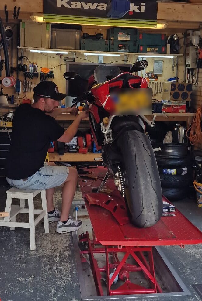 Onze monteur aan het werk aan een rode sportmotor op de heftafel in de werkplaats