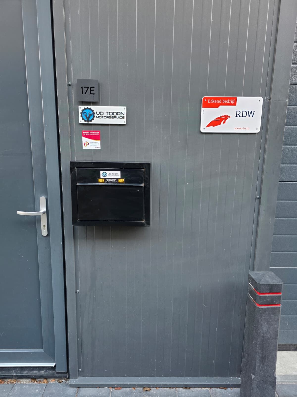 Voordeur van de werkplaats met huisnummer 17E, het RDW-bord Erkend bedrijf en de sticker Erkend leerbedrijf